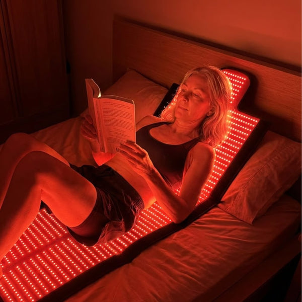 A woman reading in bed while lying on the illuminated ApolloThera Full Body Red Light Mat